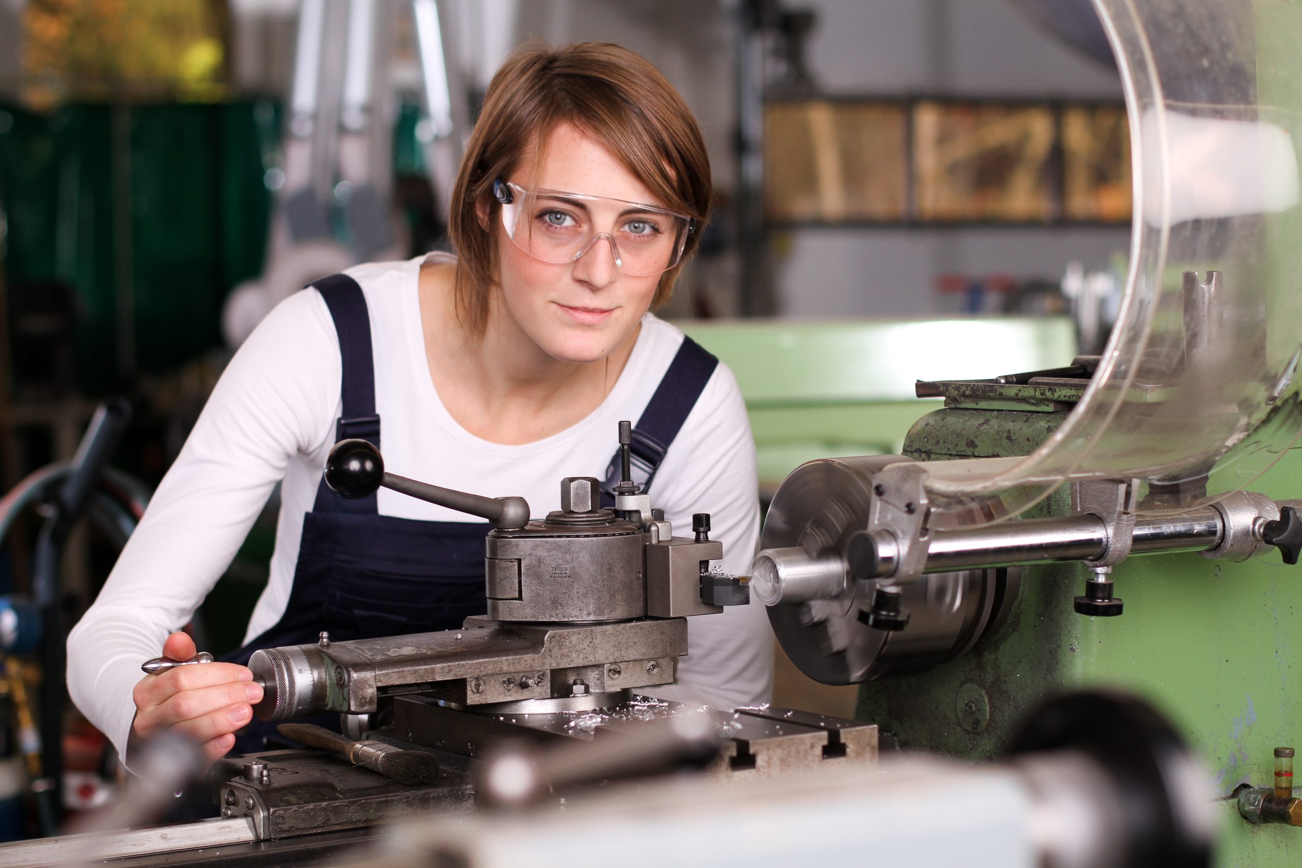 Arbeiterin in Arbeitskleidung und Schutzbrille an einer Maschine (Bild: ©ehrenberg-bilder/stock.adobe.com)